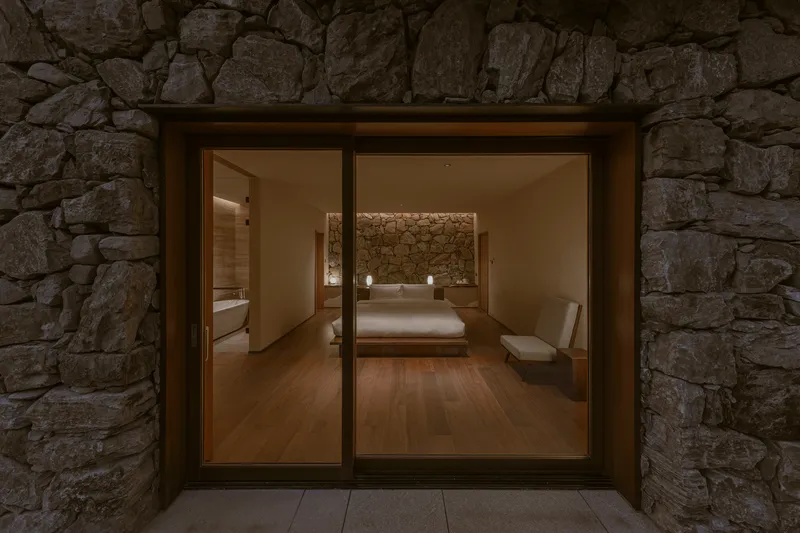 Bedroom framed by rough stone walls and viewed through sliding glass doors at night