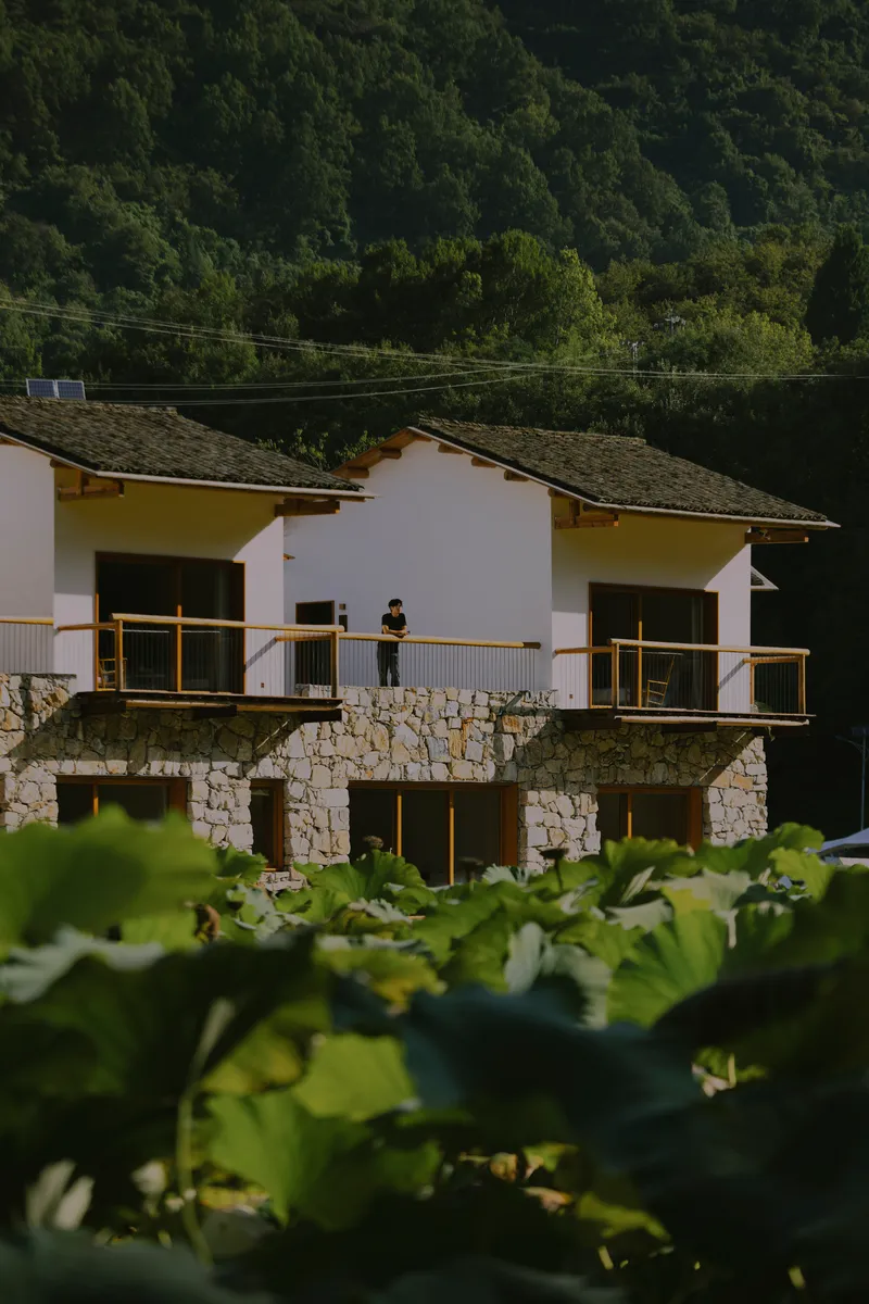 Paired gabled volumes with stone ground floors and white plaster above, a person standing on the shared balcony