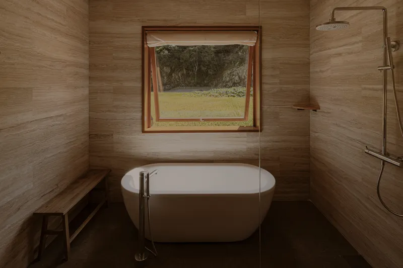 Bathroom with freestanding tub, wood-grain tile walls and casement window opening to green lawn