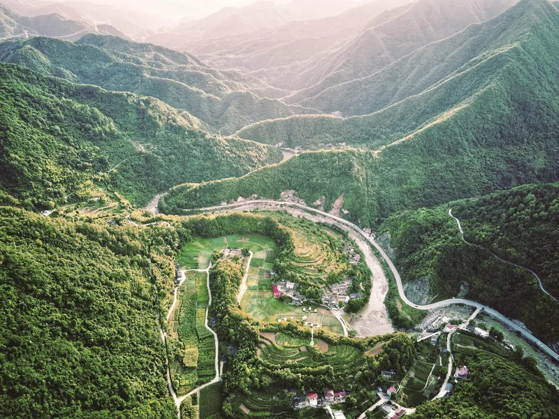 Aerial view of terraced agricultural fields and a small cluster of structures in a forested mountain valley
