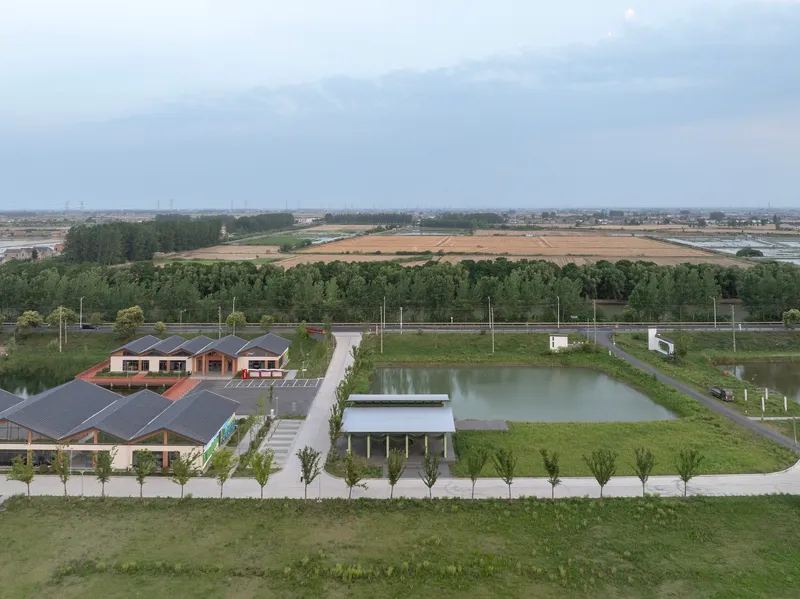 Aerial view of the site showing pavilion structures beside pond within agricultural landscape at dusk