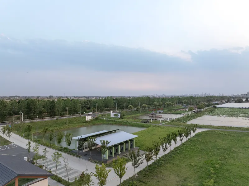 Elevated view of the pavilion with floating roof beside a pond and parking area under overcast skies