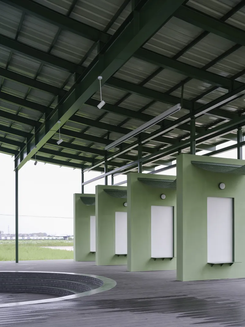 Interior view of the structural steel frame with green columns supporting the corrugated roof above exhibition panels