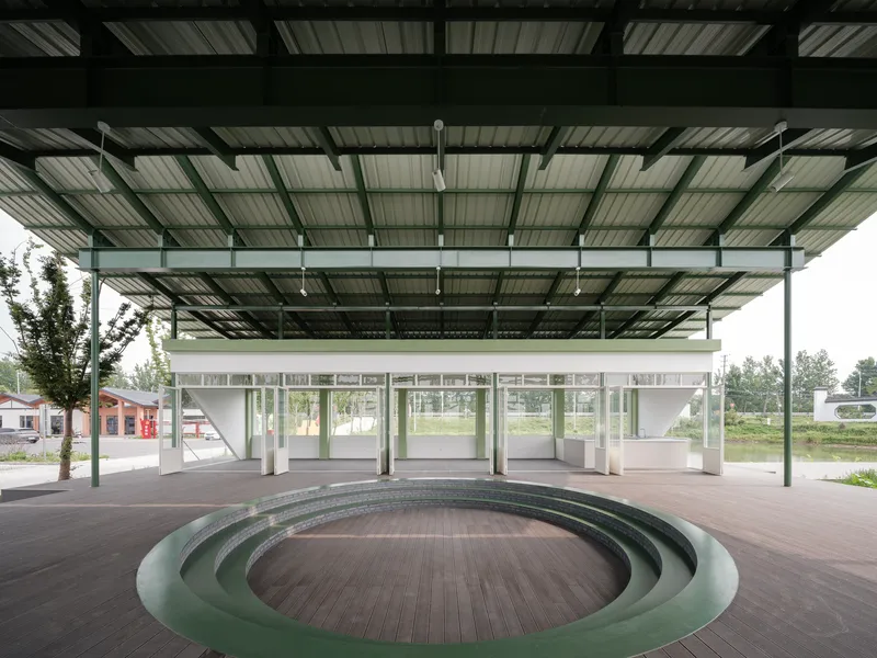 Sunken circular amphitheater beneath the open pavilion structure facing the glass-walled classroom block
