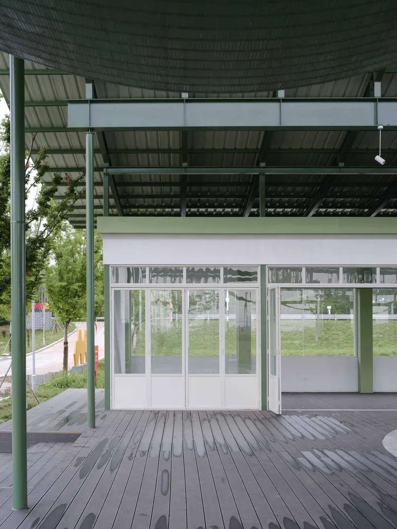 Covered deck with green steel columns and corrugated metal canopy shading glazed doors in summer