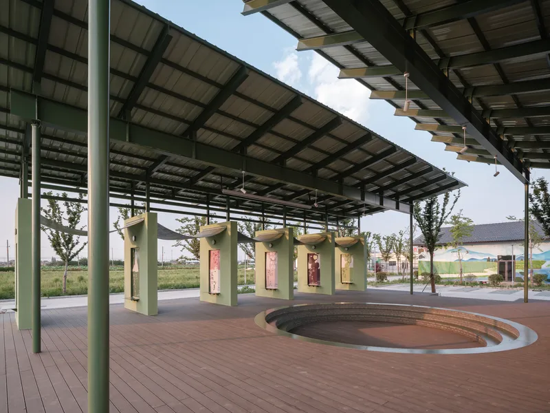 Open pavilion with solar panel roof and curved amphitheatre seating facing green exhibition kiosks