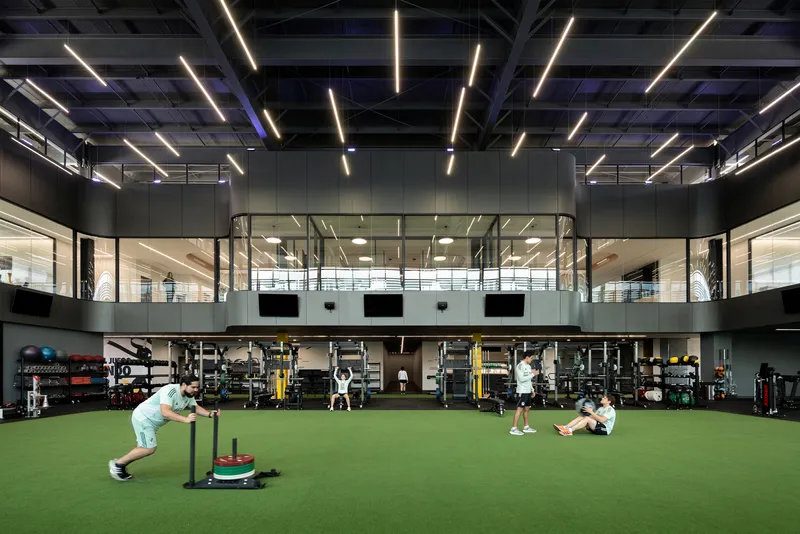 Double-height training facility with artificial turf flooring and suspended linear lighting over the exercise area