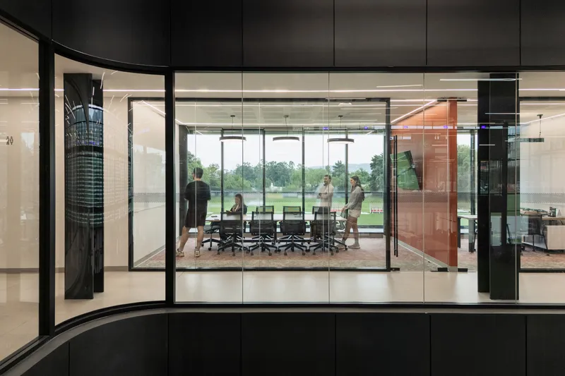 Glass conference room with pivoting red panel door overlooking a training pitch beyond