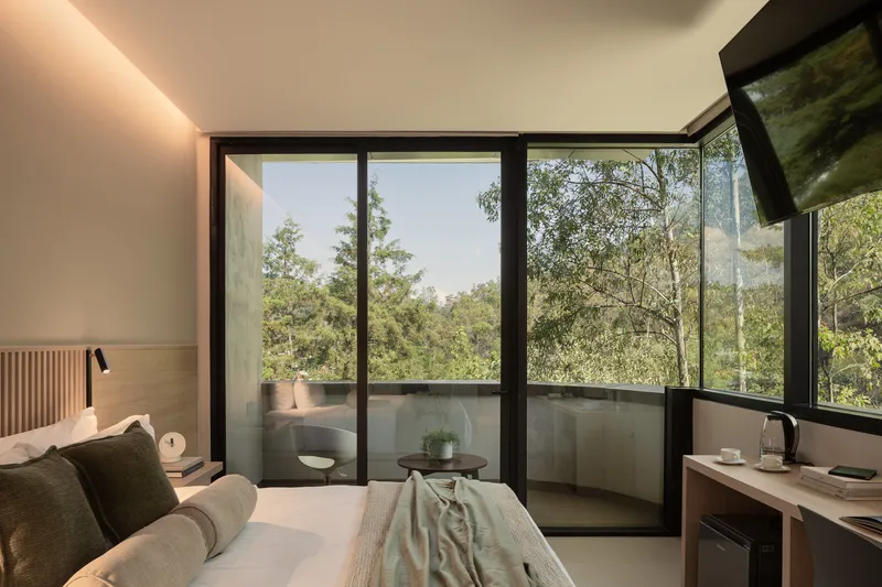 Guest room with corner glazing opening onto a small balcony framed by tree canopy