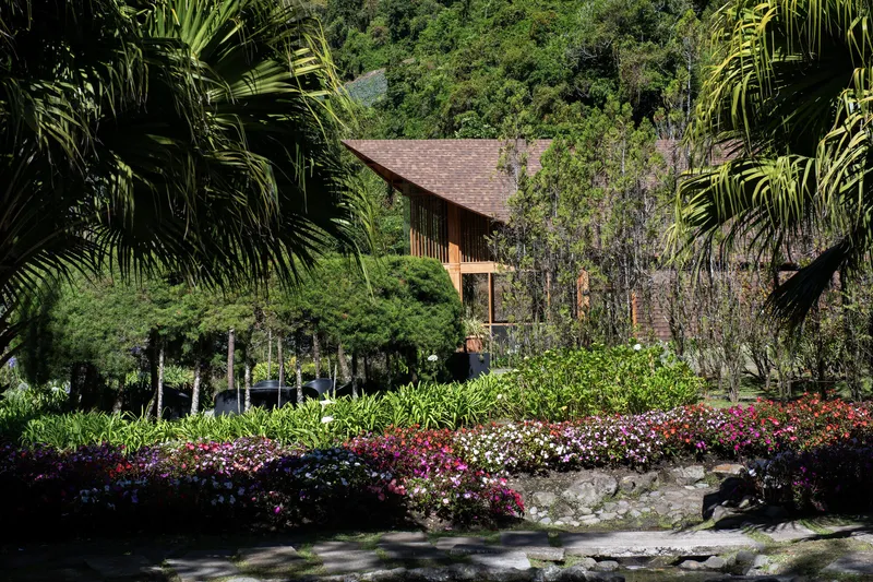 View through flowering garden beds toward the timber building with curved roof and vertical cladding