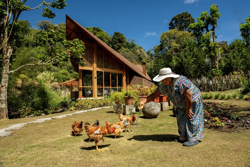 Garden view of the timber-framed facade with a woman feeding chickens on the lawn below