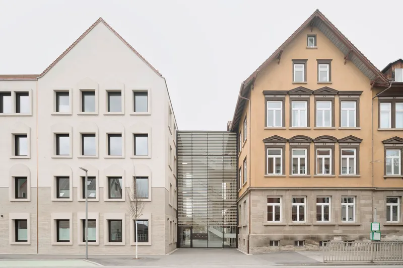 Street view showing a white gabled facade beside a traditional yellow building and a recessed metal screen connector