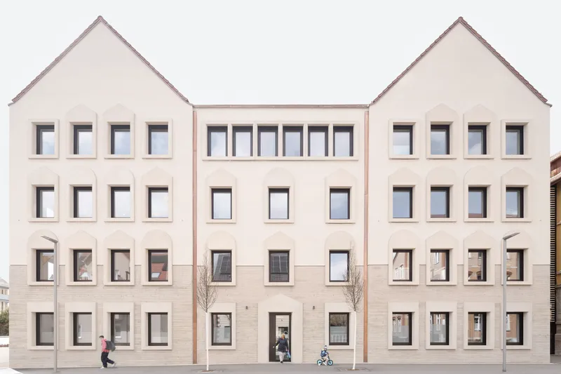 Rear courtyard facade with symmetrical gabled volumes and people walking along the ground floor with young trees