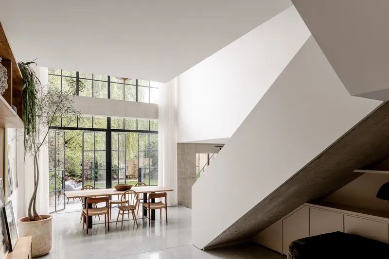Double-height dining space with angled sculptural staircase and steel-framed glazing overlooking garden