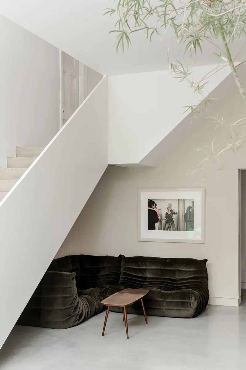 Seating nook beneath the staircase with dark velvet sofa and overhanging bamboo branches
