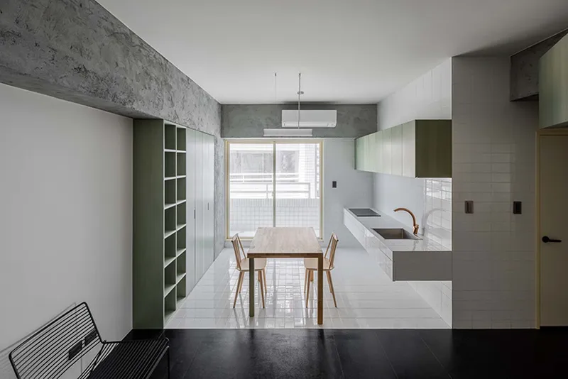 Kitchen and dining area with white tile backsplash, timber table, and pale green storage against concrete walls