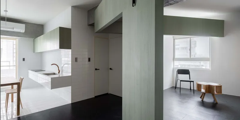 View through pale green paneled partition wall dividing the kitchen from the living zone with black flooring