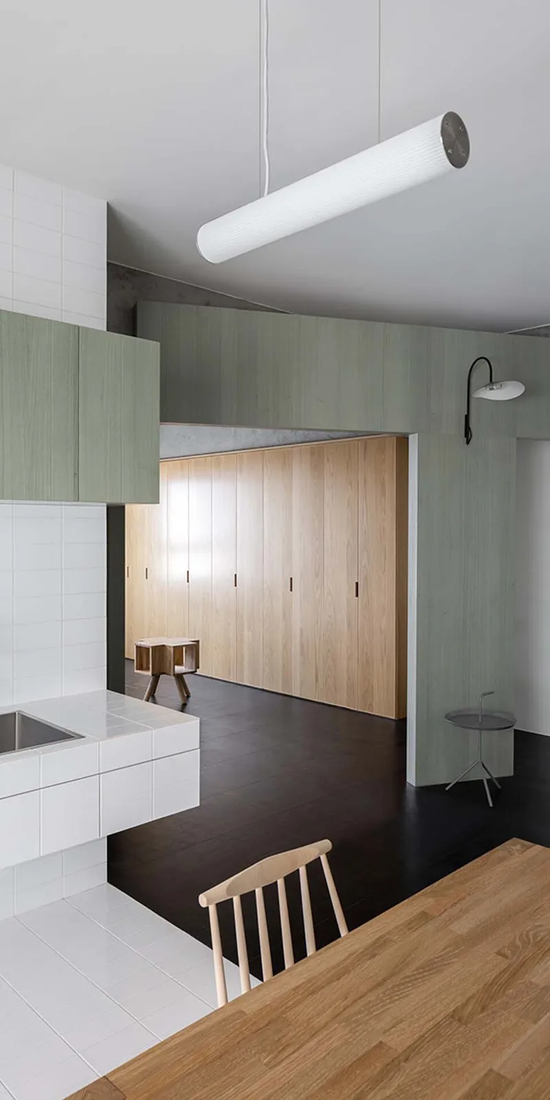 Timber wardrobe wall beneath tubular pendant light with pale green partition and black floor in foreground