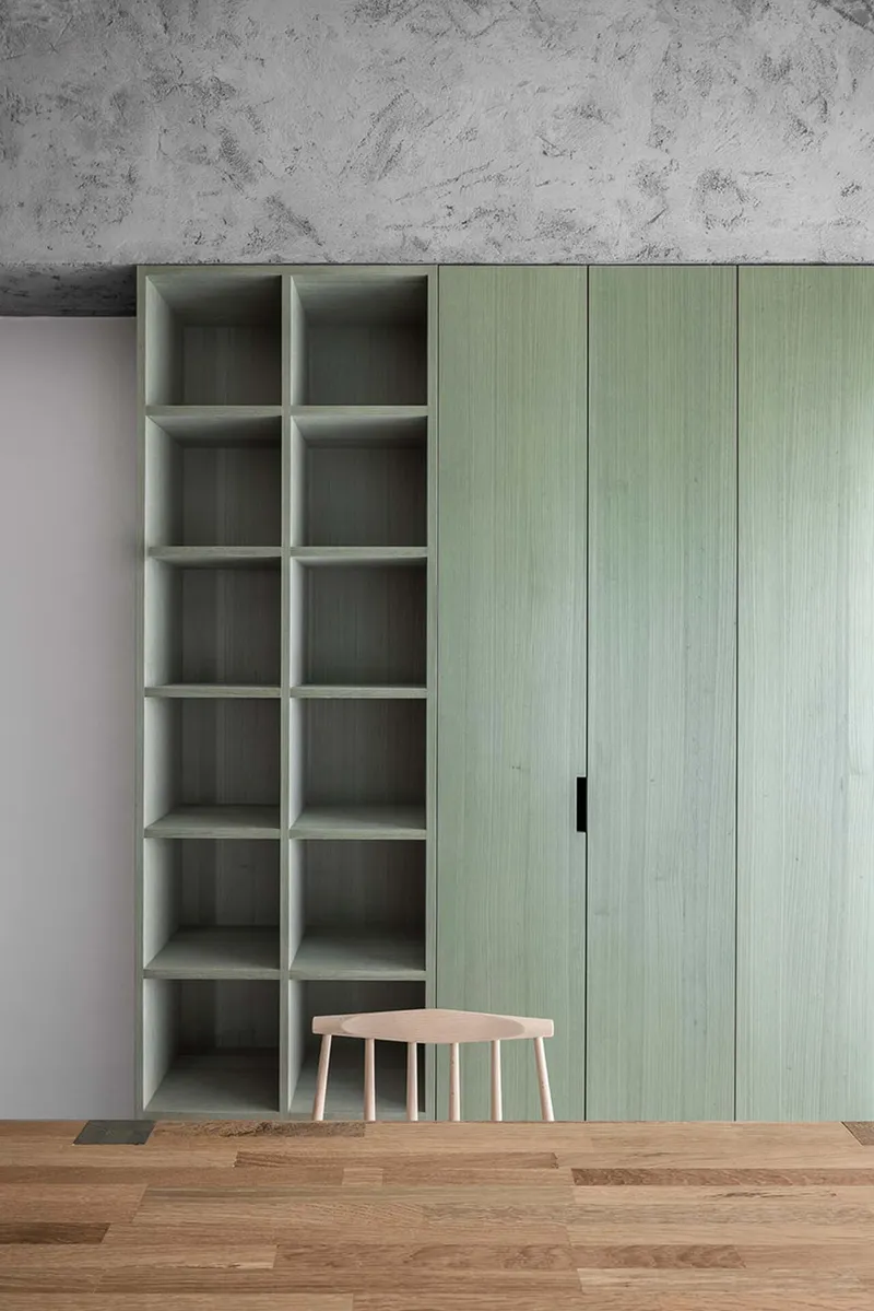 Storage wall with pale green cabinetry and open grid shelving against concrete ceiling