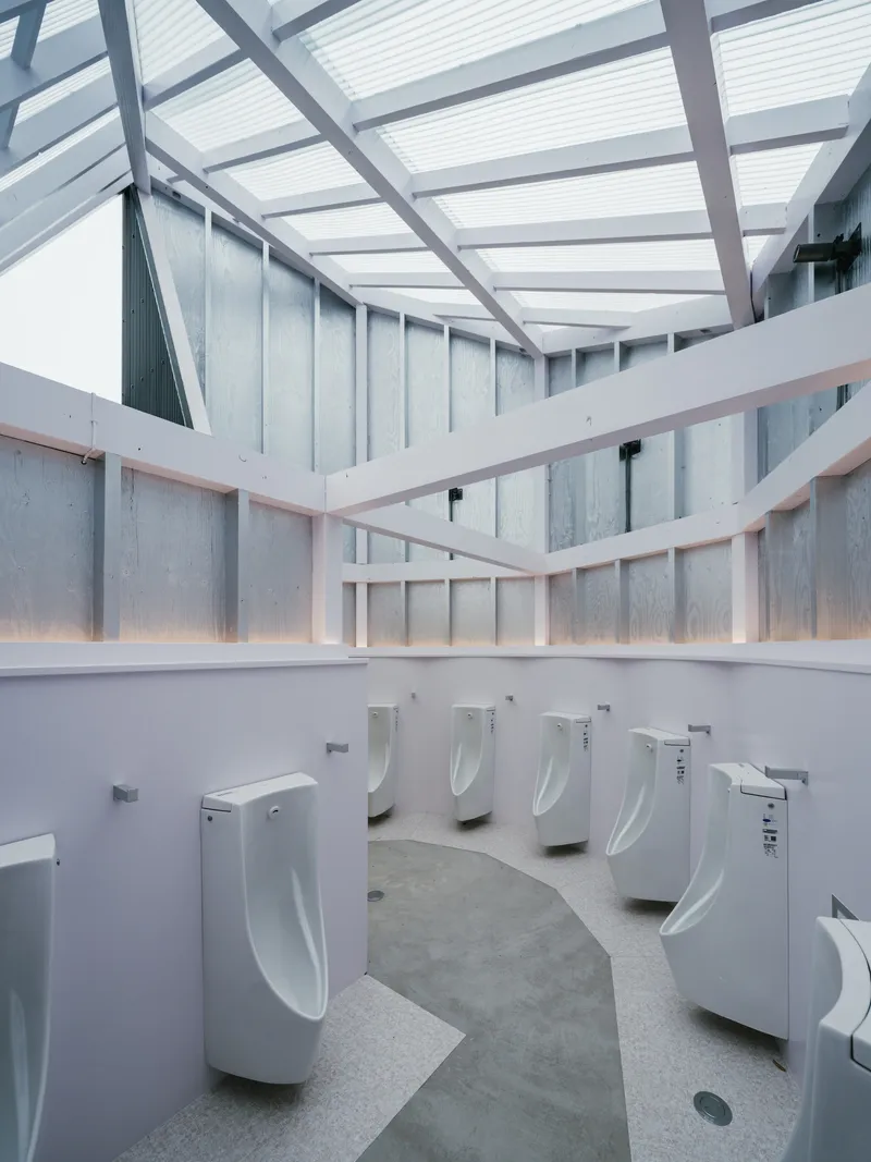 Circular restroom interior with row of white urinals beneath a translucent polycarbonate skylight and metal framing