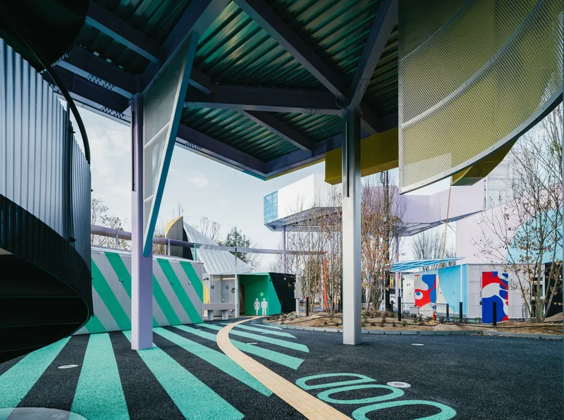 Sheltered walkway with angled corrugated roof panels and green-striped paving below bare winter trees