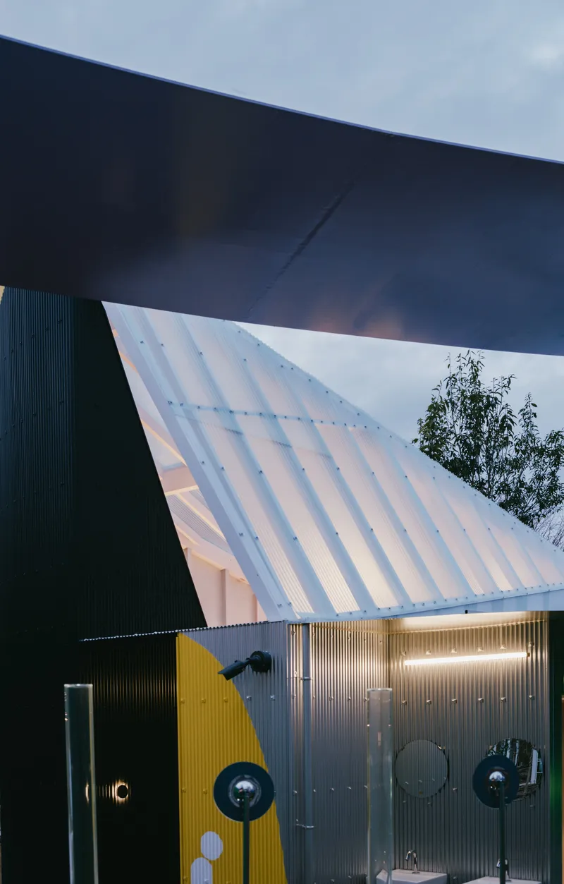Angled corrugated facade and dark overhang meeting at twilight with bare trees visible