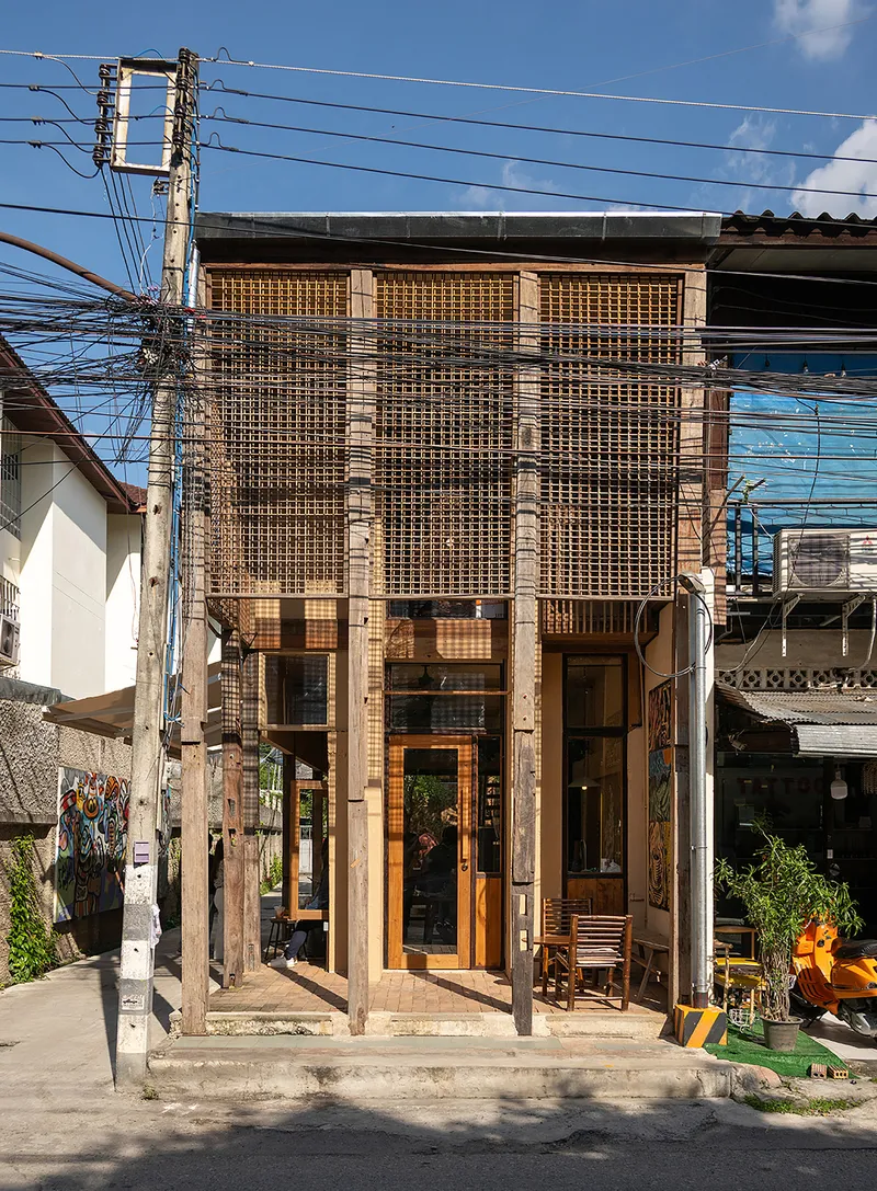 Two-story timber screen facade with brick columns on a residential street beneath overhead power lines
