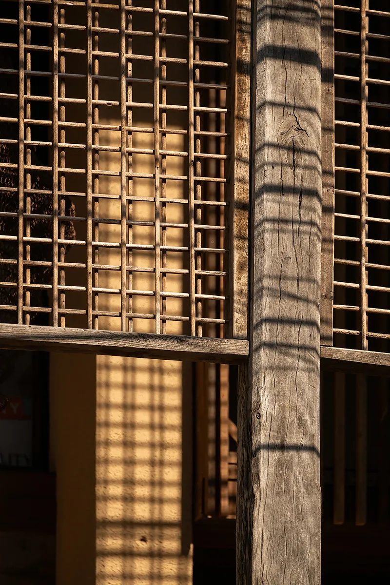 Timber column beside a wooden lattice screen casting afternoon shadow patterns on the wall