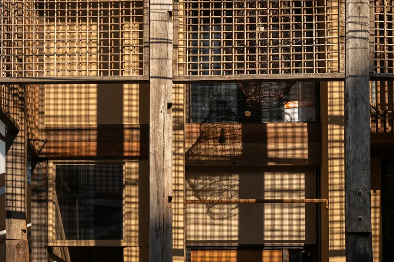 Facade with timber columns and lattice screens filtering late afternoon light across the glazing
