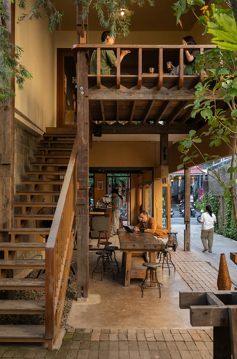 Open-tread timber staircase leading to upper mezzanine with exposed structural posts and hanging foliage