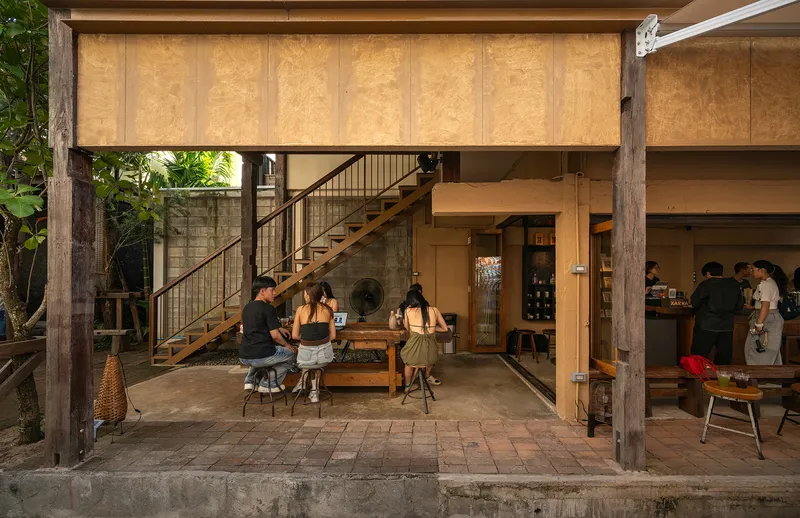 Covered terrace with timber staircase and plywood ceiling panels overlooking courtyard seating at dusk