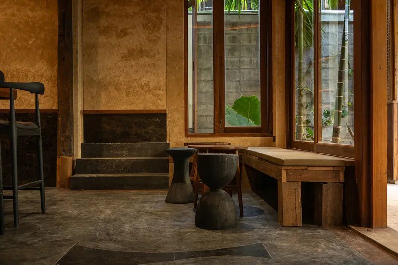 Interior stair and seating area with timber-framed windows opening onto a concrete-walled courtyard with tropical plants