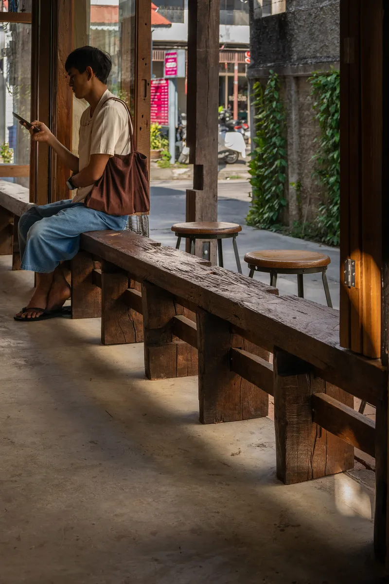 Timber bench and stools along the interior threshold where a person sits reading in natural daylight
