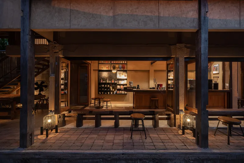 Street view of the open pavilion framed by timber columns with dining platform and interior bar at twilight