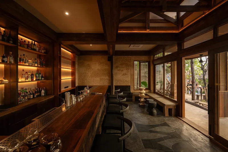 Interior bar with backlit shelving, timber post-and-beam structure and glazed doors overlooking a planted garden