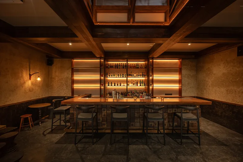 Bar interior with timber-beamed coffered ceiling, skylights, backlit bottle shelves and stools around a counter