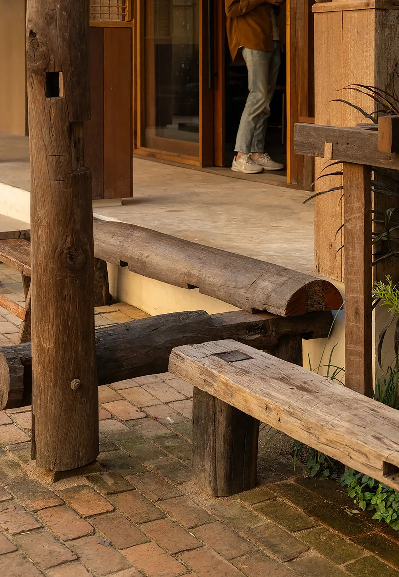 Reclaimed timber bench and columns on a brick paved terrace with a person entering through glazed doors