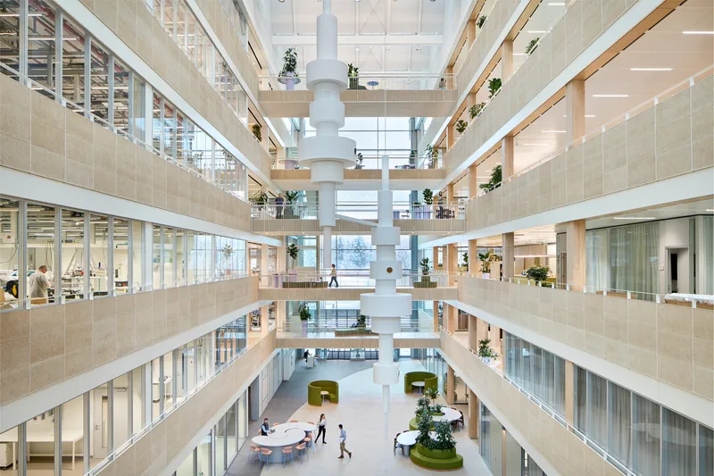 Multi-story atrium with central white column, timber-clad balconies and potted plants on each floor
