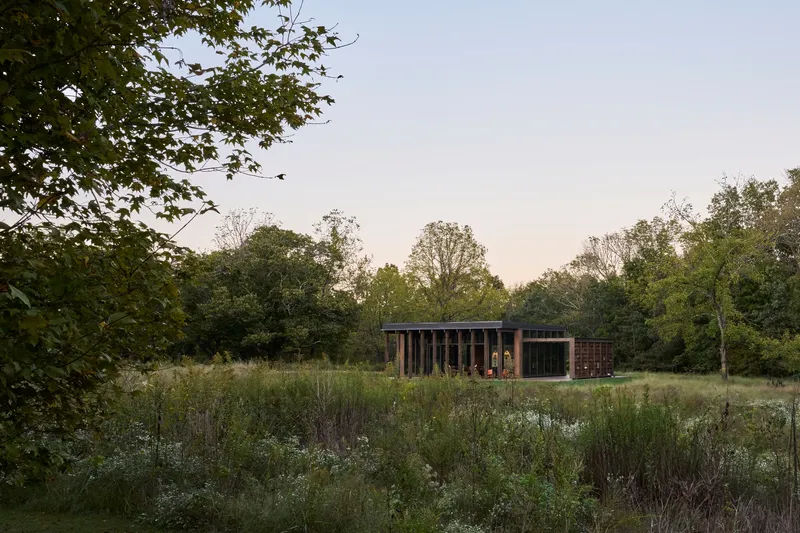 Pavilion with vertical timber cladding and slatted screens set in a wildflower meadow at dusk