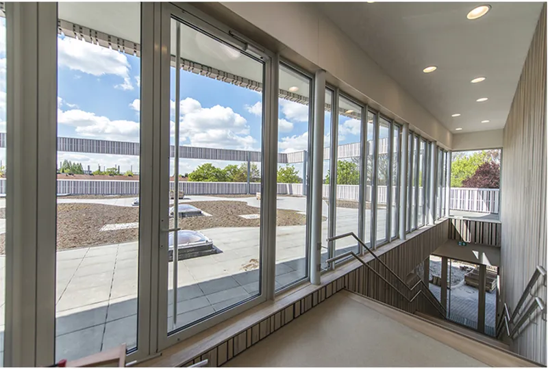 Large windows connect the school interior to roof terraces, daylight, and the surrounding green landscape.
