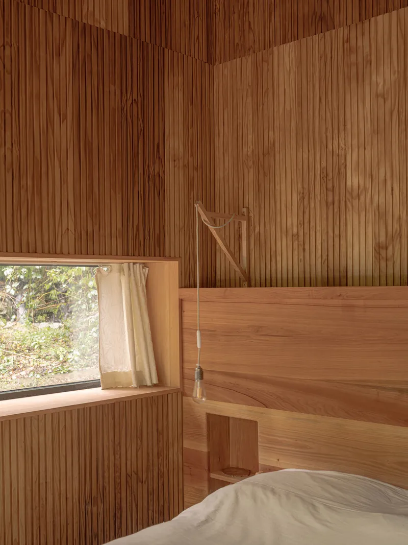 Bedroom with vertical timber slat walls and ceiling, a wood-framed bed and a window framing foliage outside