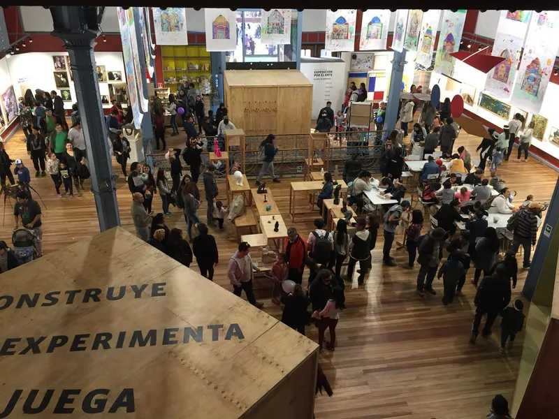 Overhead view of the crowded exhibition hall with wooden displays and visitors gathered around workshop tables