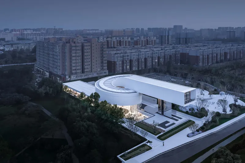 Aerial view of the curved roof with circular skylight and green courtyards at dusk