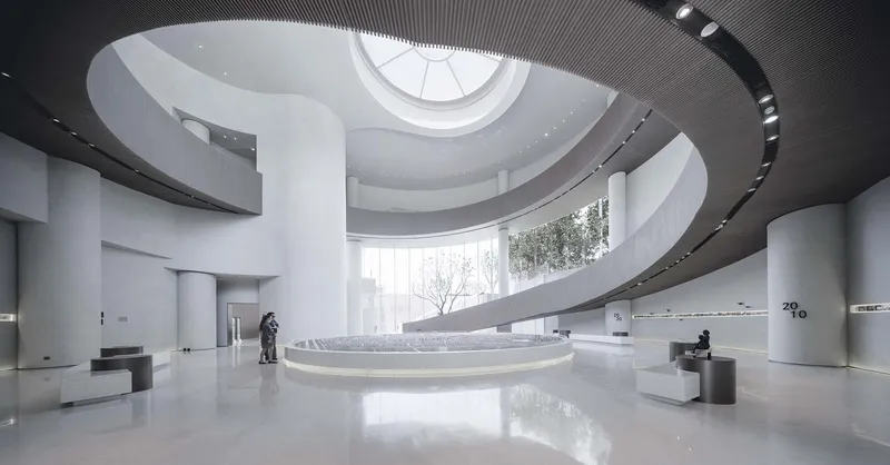 Double-height atrium with spiraling ramp around a circular skylight and visitors below