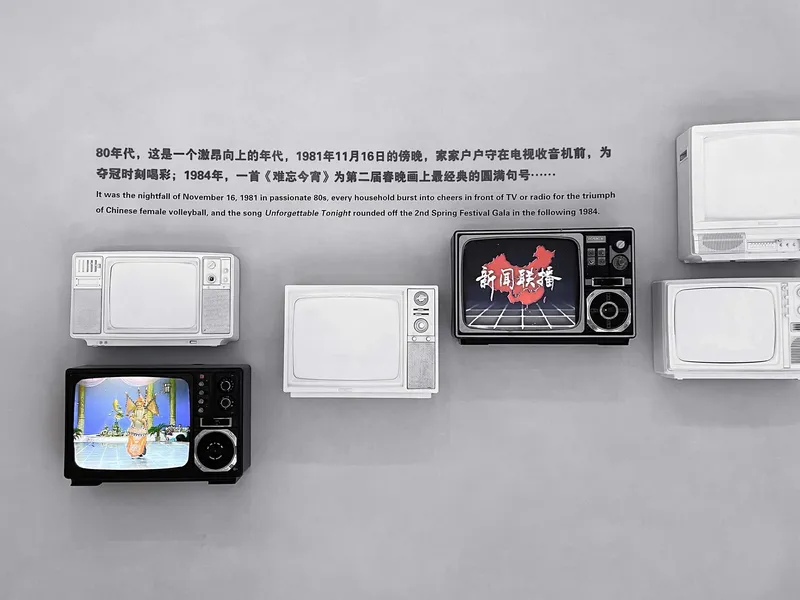 Wall display of vintage television sets mounted on a grey surface with Chinese text above