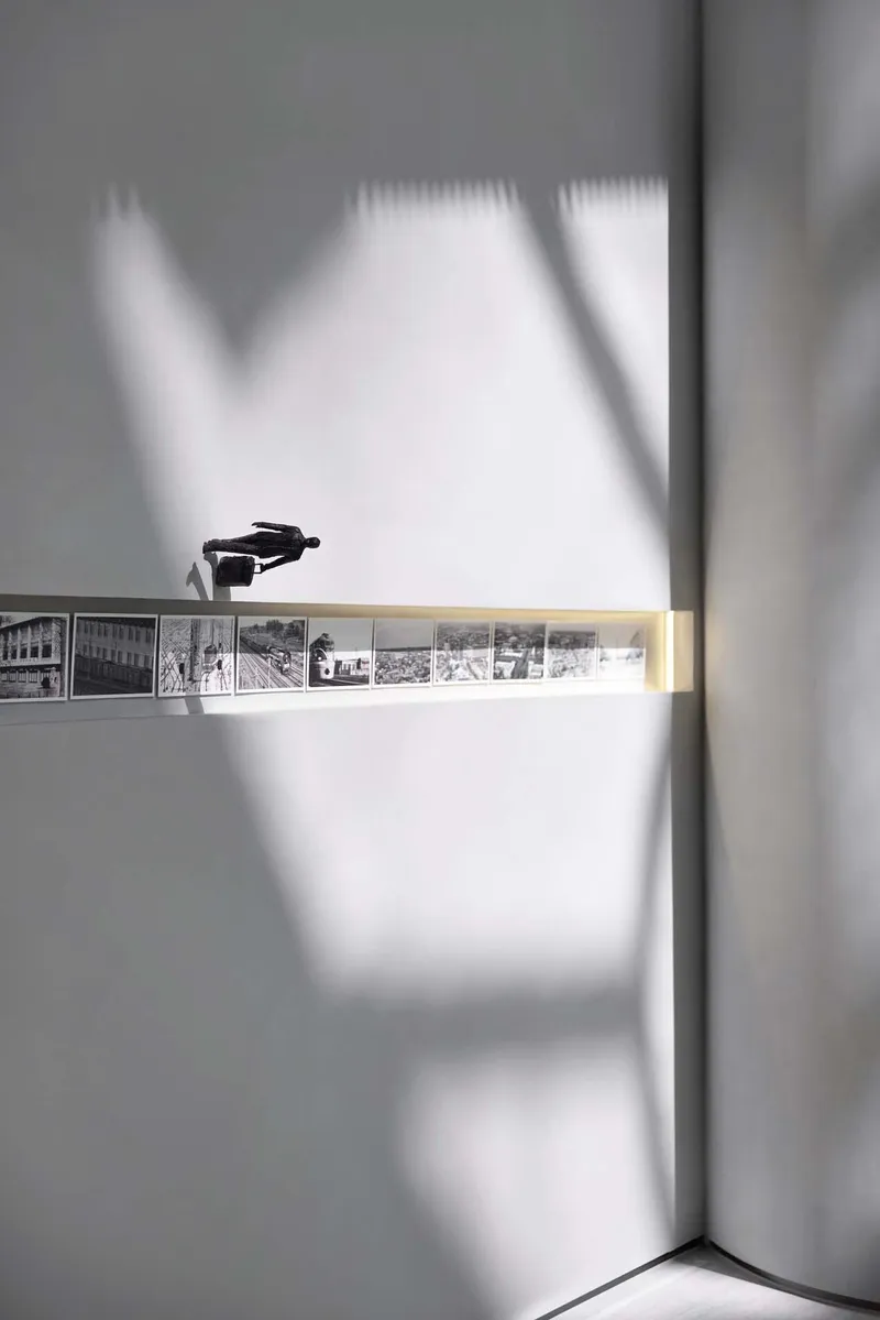 Corner detail of illuminated horizontal display strip with archival photographs casting shadows on white walls