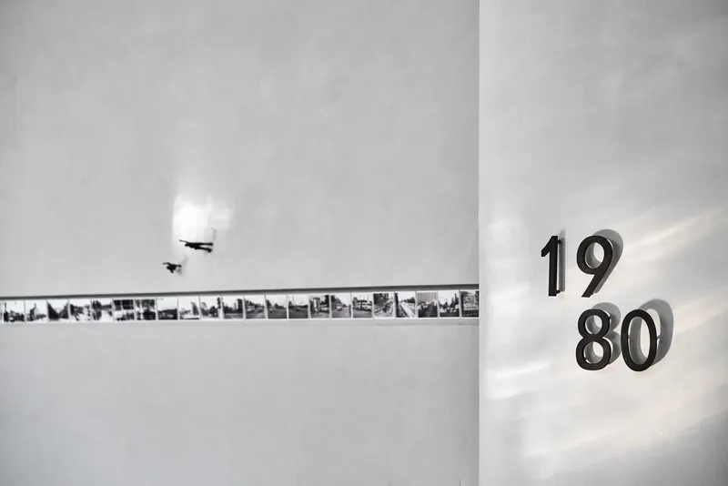 Wall detail showing backlit numerals reading 1980 beside a horizontal strip of archival photographs