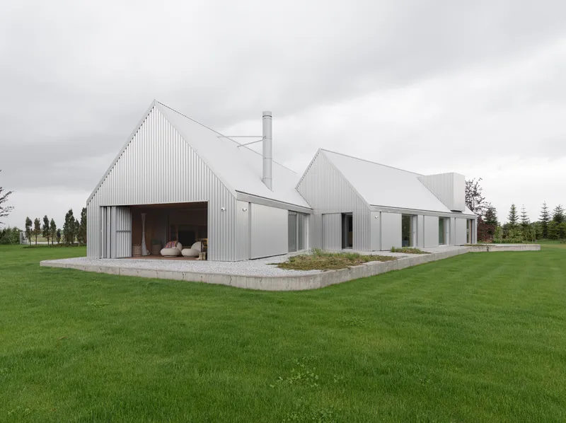 Cluster of corrugated metal gabled volumes on a concrete plinth surrounded by lawn under overcast skies