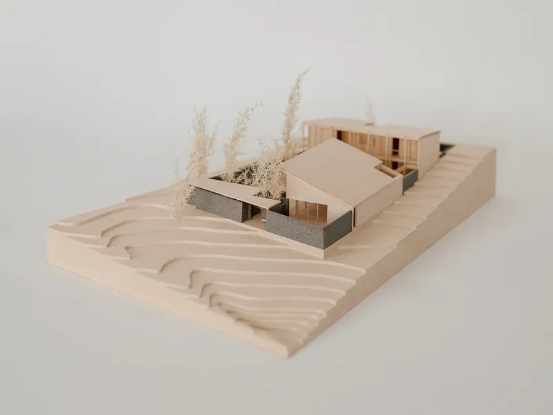 Wooden site model showing two gabled volumes with planted courtyard on contoured topography