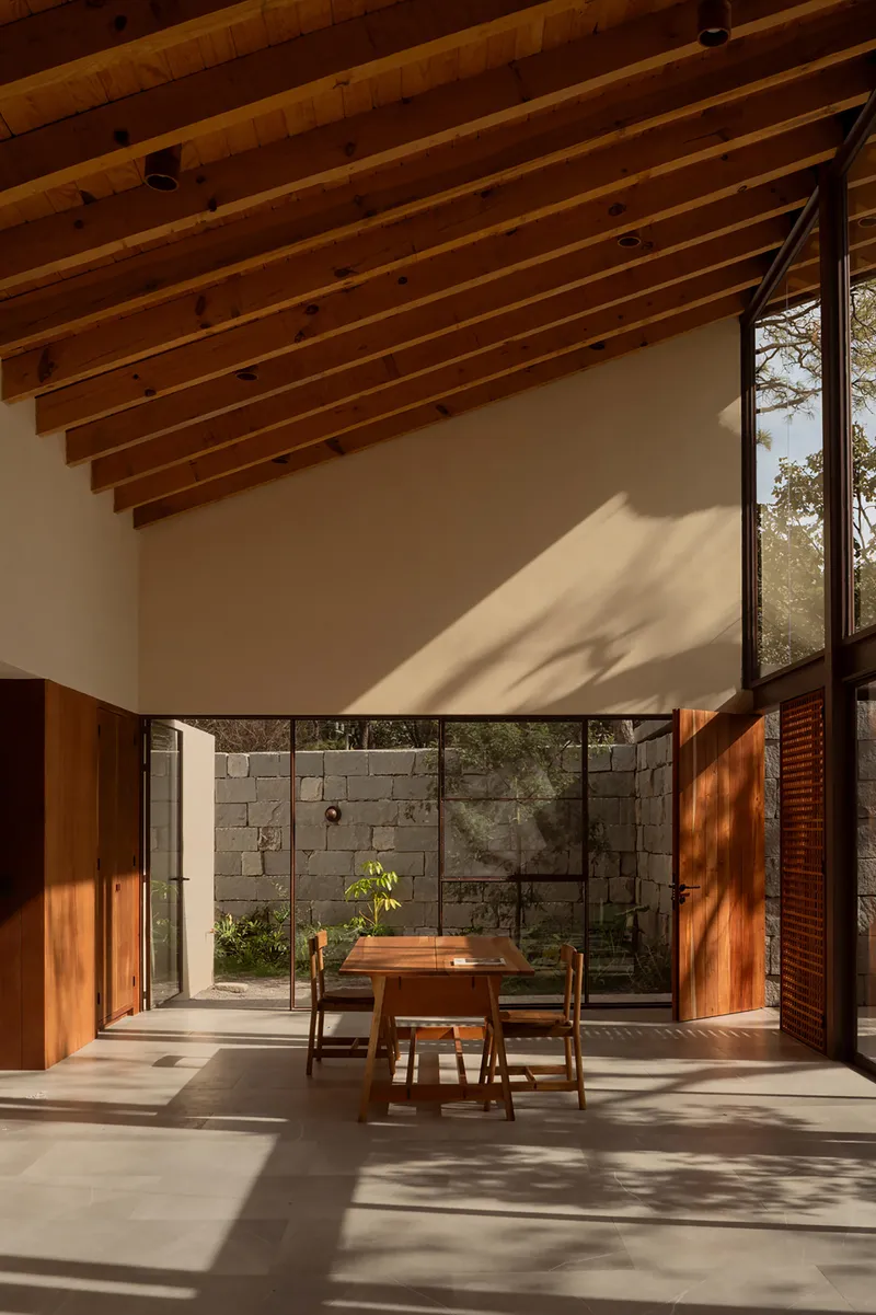 Dining area with exposed timber rafters and dappled afternoon sunlight across the concrete floor